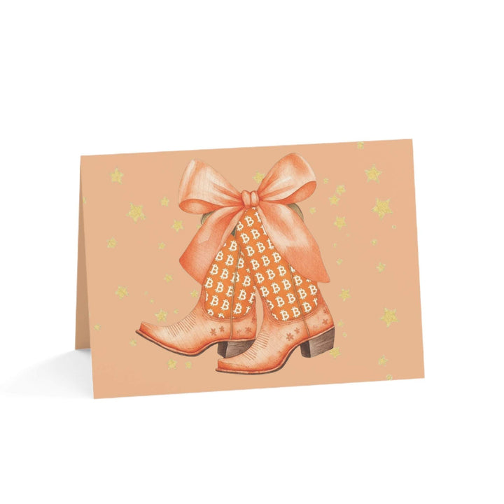Watercolor Bitcoin Boots greeting card with orange boots, golden Bitcoin patterns, and a bow on peach background with stars